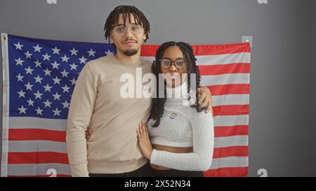 Ein Mann und eine Frau mit Aufklebern "ich habe gestimmt", die vor einer amerikanischen Flagge stehen und die bürgerliche Pflicht und Partnerschaft darstellen. Stockfoto