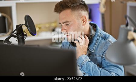 Fokussierter hispanischer Mann mit Kopfhörern im Musikstudio in der Nähe von Mikrofon und Instrumenten Stockfoto