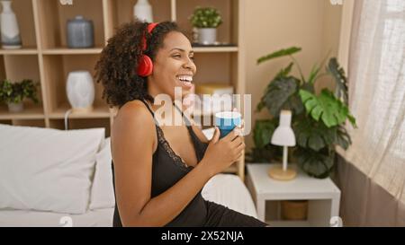 afroamerikanerin mit Kopfhörern genießt Musik in ihrem Schlafzimmer und hält einen Becher Stockfoto