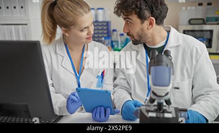 Ein Mann und eine Wissenschaftlerin arbeiten in einem Labor zusammen, analysieren Daten auf einem Tablet, umgeben von wissenschaftlichen Geräten. Stockfoto