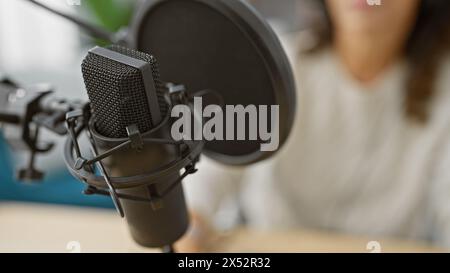 Fokussierte Frau nimmt Podcasts mit professionellem Mikrofon in einem modernen Studio auf. Stockfoto