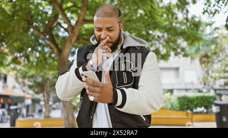 Ein nachdenklicher afroamerikaner mit Bart überprüft sein Smartphone in einem Stadtpark. Stockfoto