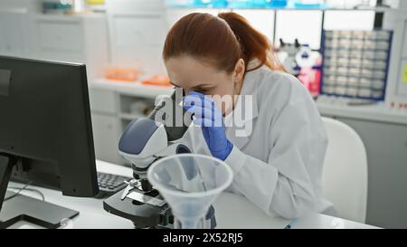 Eine fokussierte kaukasische Wissenschaftlerin, die Proben mit einem Mikroskop im Labor analysiert Stockfoto