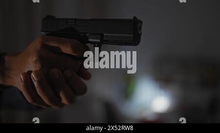 Nahaufnahme eines nicht erkennbaren Mannes, der eine Handfeuerwaffe hält, mit Fokus auf die Waffe, was auf ein spannendes Indoor-Szenario hindeutet. Stockfoto