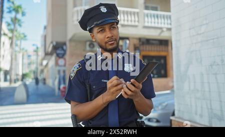 afroamerikanischer Polizist macht Notizen auf einem Tablet in einer sonnigen städtischen Straßenszene Stockfoto