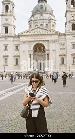 Eine stilvolle Latina-Frau benutzt ein Smartphone vor budapester Straße. stephans Basilika Stockfoto