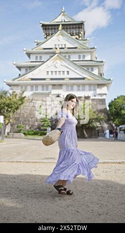 Wunderschöne hispanische Frau, die sich in einem atemberaubenden Kleid um das alte Schloss osaka dreht - ein heiteres Urlaubs-Highlight inmitten japanischer Tradition Stockfoto