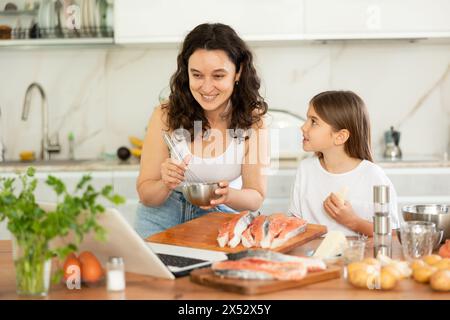 Glückliche Mutter und Tochter bereiten Lachs in der Küche vor Stockfoto