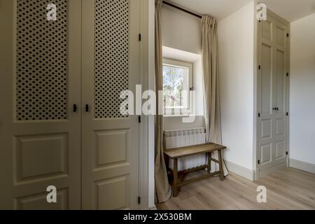 Neu renoviertes Schlafzimmer mit Einbauschränken mit Gittertüren und einem quadratischen Fenster in der Mitte Stockfoto