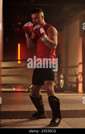 Aufnahme eines jungen aktiven Mannes in Sportbekleidung, der auf dem Boden des Boxrings steht und Übungen für bevorstehende Wettkämpfe übt Stockfoto