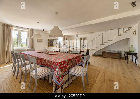 Ein großes Wohnzimmer mit Kamin mit Esstisch mit roter Tischdecke, Holzfußboden, eingebauter Treppe und wunderschönem zeitgenössischen Dekor Stockfoto
