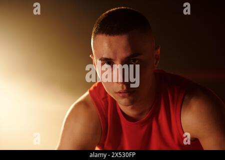 Junger Sportler in roter Sportbekleidung, der nach dem Training vor der Kamera auf dem Boxring steht und dich gegen Licht und Rauch ansieht Stockfoto