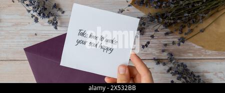 NEHMEN SIE SICH DIE ZEIT, UM IHRE SEELE GLÜCKLICH ZU MACHEN, indem Sie auf einer unterstützenden Nachricht auf Papier Notizen aus dem grünen Umschlag erinnern. Flache Zusammensetzung trockene Lavendelblüten. Konzept von innerem Glück, Verlangsamung digitaler Detox persönliche Erfüllung. Draufsicht Stockfoto