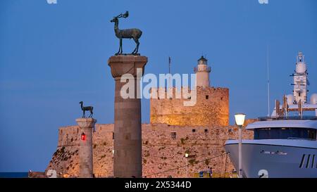 Eine Hirschskulptur auf einer Säule vor einer Burg und einem Leuchtturm neben einer Luxusyacht in der Abenddämmerung, Hirschstatue, Hirschstatue, Fort Agios Nikolaos Stockfoto