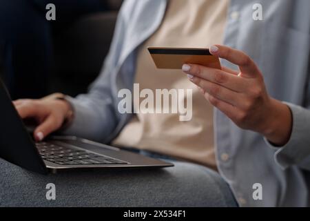 Hand einer jungen, nicht erkennbaren Frau mit Kreditkarte und Laptop, während sie vor der Kamera sitzt und online bezahlt Stockfoto