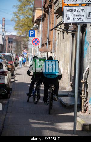 Zwei Fahrradkuriere mit Lieferrucksäcken fahren auf einer Stadtstraße in Riga, Lettland Stockfoto