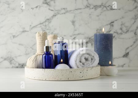 Spa-Zusammensetzung. Flaschen mit Kosmetikprodukten, Handtuch, Kräuterbeutel und brennende Kerzen auf weißem Holztisch Stockfoto