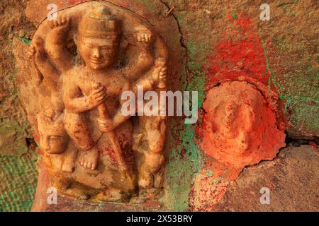 BAS-Relief einer verwitterten Marmor-Gottheit, eingebettet in eine Wand neben einem stark bemalten orangen Ganesh in Varanasi, Indien. Stockfoto