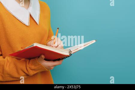 Zurück zur Schule. Mädchen mit Arbeitsbuch auf dem Hintergrund einer hellen blaugrünen Wand. Stockfoto