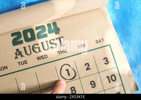 Hand zeigt auf das Datum vom 1. August 2024 auf der flachen Kalenderfläche mit blauem Hintergrund. Erinnerung am ersten Augusttag. Stockfoto