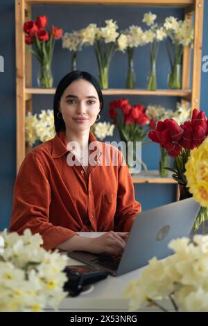 Eine Floristin steht an der Theke ihres Blumengeschäfts und nimmt mit dem Laptop Bestellungen für ihren Laden entgegen. Stockfoto