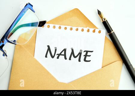 Ein Wort namens eine Inschrift auf einem Stück Papier, das aus einem Umschlag neben Gläsern und Bleistiften blickt Stockfoto