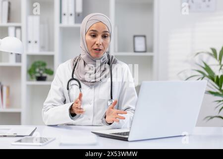 Eine professionelle muslimische Ärztin in einem Hijab, die Gesundheitsoptionen erklärte, saß an ihrem Schreibtisch in einem hellen, modernen Klinikbüro. Sie sieht engagiert und sachkundig aus. Stockfoto