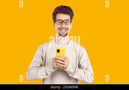Porträt eines glücklichen jungen Mannes in lässigen Kleidern, der das Handy in den Händen hält. Stockfoto