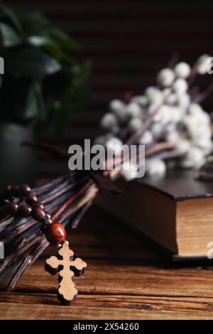 Rosenkranzperlen, Bibel und Weidenzweige auf Holztisch, Nahaufnahme Stockfoto