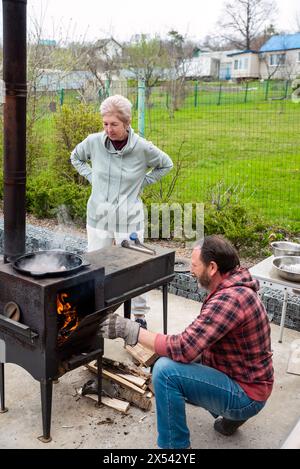 Reifer russischer Mann und Frau, die Fleisch in einem Kessel auf dem Herd im Freien braten, Familienkonzept Stockfoto