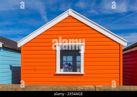 Farbenfrohe orange Strandhütte mit Blick auf das Meer und RNLI Lifeboat Flaggen im Fenster in Southwold, Suffolk, Großbritannien im April Stockfoto