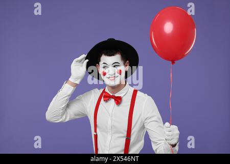 Lustiger Mime-Künstler mit rotem Ballon auf violettem Hintergrund Stockfoto