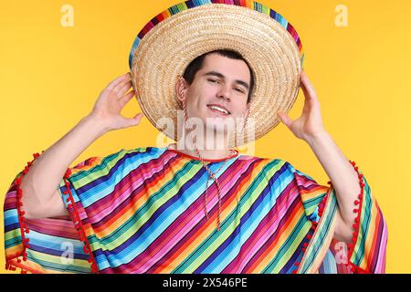 Junger Mann mit mexikanischem Sombrero-Hut und Poncho auf gelbem Hintergrund Stockfoto