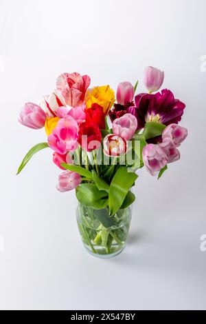 Eine Vase gefüllt mit einer Vielzahl von bunten Blumen, darunter rosa, gelbe und rote Tulpen, die auf einem weißen Tisch sitzen. Stockfoto