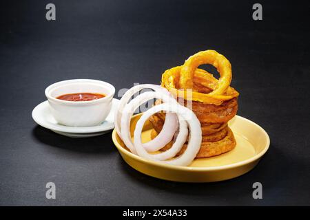 Hausgemachte knusprige Zwiebelringe mit Tomatensauce und rohen Zwiebelscheiben. Snacks am Abend. Stockfoto