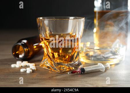 Alkohol- und Drogensucht. Whiskey in Glas, Spritze, Pillen und Zigaretten auf Holztisch Stockfoto