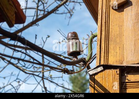 Porzellan-Isolator für Elektrodrähte gegen blauen Himmel an der Wand eines Holzhauses. Stockfoto