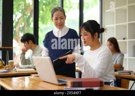 Freundliche Professorin, die Studentin bei der Aufgabe hilft Stockfoto