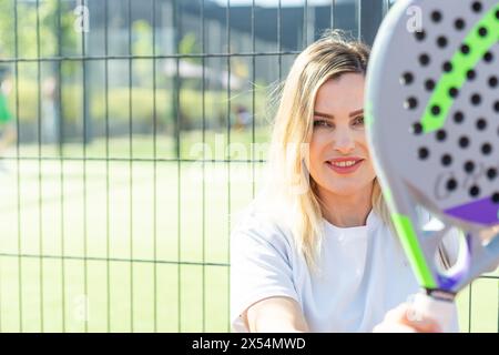 Ukraine Kiew, 03. Mai 2024. Porträt einer lächelnden Frau mit Padel-Tennisschlägerkopf auf dem Hof Stockfoto