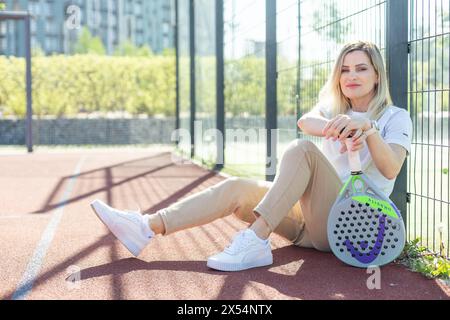 Ukraine Kiew, 03. Mai 2024. Porträt einer lächelnden Frau mit Padel-Tennisschlägerkopf auf dem Hof Stockfoto