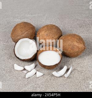 Kokosmilch in Kokosnussschale und Kokosnuss, gehacktes Fleisch auf grauem Hintergrund Stockfoto
