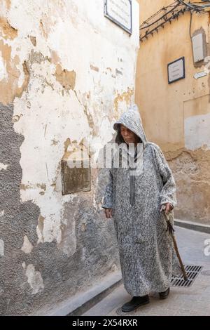 Ein älterer Mann in einer Djellaba geht durch eine alte Gasse in Fès, Marokko. Stockfoto