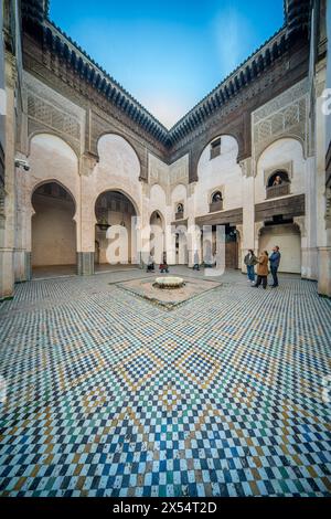 Besucher im kunstvollen Innenhof von Madrasa Cherratine unter einem klaren blauen Himmel. Stockfoto