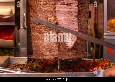 Nahaufnahme eines Küchenchefs, der Fleisch mit einem Dönermesser für einen traditionellen Street Food Döner oder Shawarma schneidet. Konzept des Street Food Stockfoto