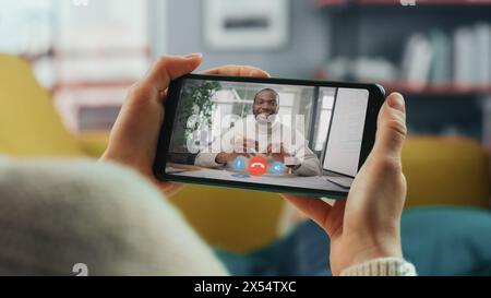 Junge Frau chatte in einem Videoanruf mit ihrem gutaussehenden männlichen afroamerikanischen Freund auf dem Smartphone von Home Living Room. Arbeiten Sie mit dem Home Specialist und tätigen Sie einen Anruf mit dem Manager über das Internet. Stockfoto