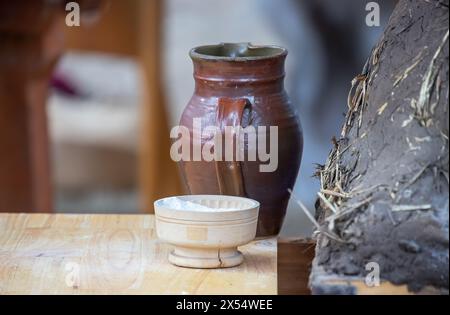 Keramikkkanne, Schüssel mit Mehl und mittelalterlicher Lehmofen zum Brotbacken aus der Nähe, Geschirr auf einem Holztisch, mittelalterlicher Lebensstil, Stillleben. Stockfoto