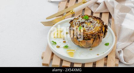 Köstliche gebackene Artischocke mit Parmesankäse und Pistazien. Olivenöl, Knoblauch, Petersilie und Zitrone. Weißer hölzerner Hintergrund, verzehrfertig vegane Speisen, Stockfoto