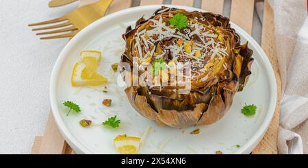 Köstliche gebackene Artischocke mit Parmesankäse und Pistazien. Olivenöl, Knoblauch, Petersilie und Zitrone. Weißer hölzerner Hintergrund, verzehrfertig vegane Speisen, Stockfoto