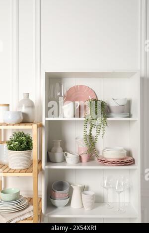 Verschiedene saubere Geschirr und Zimmerpflanzen auf den Regalen im Schrank drinnen Stockfoto