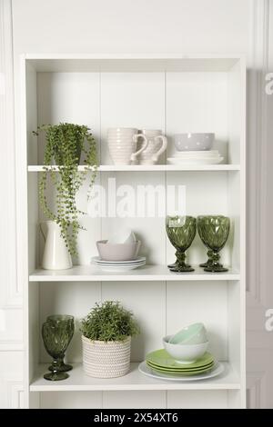 Verschiedene saubere Geschirr und Zimmerpflanzen auf den Regalen im Schrank drinnen Stockfoto